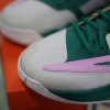 Hình ảnh cận cảnh của một đôi giày bóng rổ nam Nike Giannis Immortality 3 5 The Hard Way DZ7533-300 màu xanh lá cây và trắng với điểm nhấn màu hồng. Đôi giày có họa tiết khâu phức tạp và được đặt trên một hộp giày màu cam. Lưu bản nháp tự động nắm bắt được bản chất một cách hoàn hảo, mặc dù cảnh hơi mờ ở phía sau.