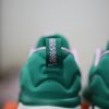 Cận cảnh phần gót giày của một đôi giày thể thao Nike Giannis Immortality 3 5 The Hard Way màu xanh lá cây với điểm nhấn màu hồng. Đôi giày có một thẻ ở gót giày với dòng chữ 