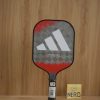 Vợt Pickleball Adidas Adipower Ctrl 3.2 PB1CA0 5 Vợt Pickleball Adidas Adipower Ctrl đặt nghiêng cho thấy họa tiết kẻ ca-rô, đầu vợt màu đỏ cam cán vợt màu đen